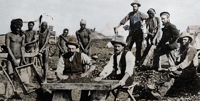 Black_and_white_miners_around_a_diamond_sorting_table._Kimberley,_South_Africa,_1800s.jpg